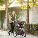 Load image into gallery viewer, A mom is pushing her child in the Baby Trend XCEL-R8 PLUS Jogger Stroller with LED