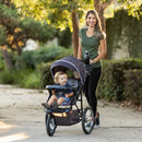 Load image into gallery viewer, A mom is pushing her child in the Baby Trend XCEL-R8 PLUS Jogger Stroller with LED
