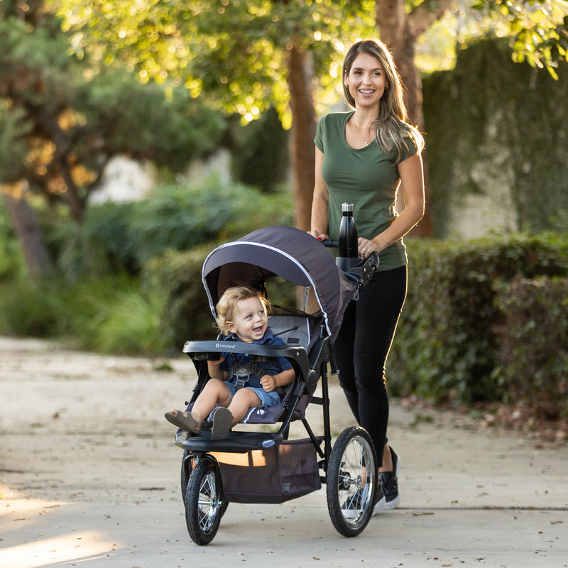 A mom is pushing her child in the Baby Trend XCEL-R8 PLUS Jogger Stroller with LED