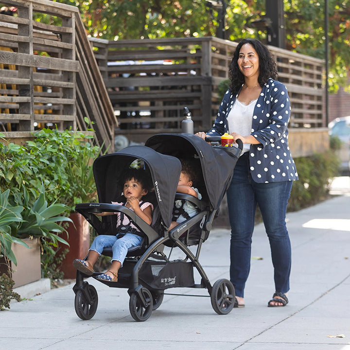 A mom is pushing her two children in the Baby Trend Sit N Stand double stroller